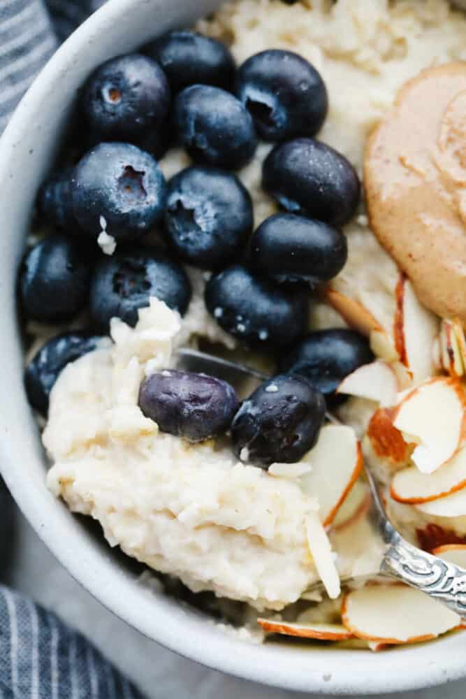 A warm, tasty bowl of homemade oatmeal is the perfect way to start your day! Here are 4 yummy variations filled with fresh fruit, nuts, brown sugar, and more! A closeup of oatmeal topped with blueberries, almonds, and nut butter.