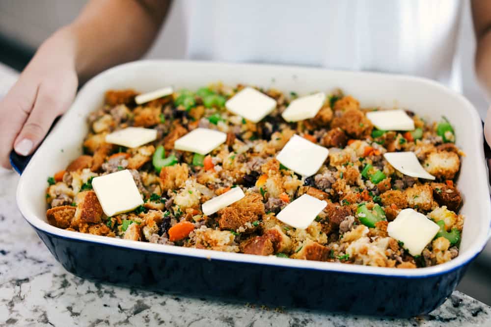 Grandma's sausage herb stuffing is a classic side dish! Baked bread, tender sausage, and crunchy vegetables are all mixed with flavorful herbs and baked until golden brown. It makes my mouth water just thinking about it! sausage herb stuffing in a baking dish with butter overtop