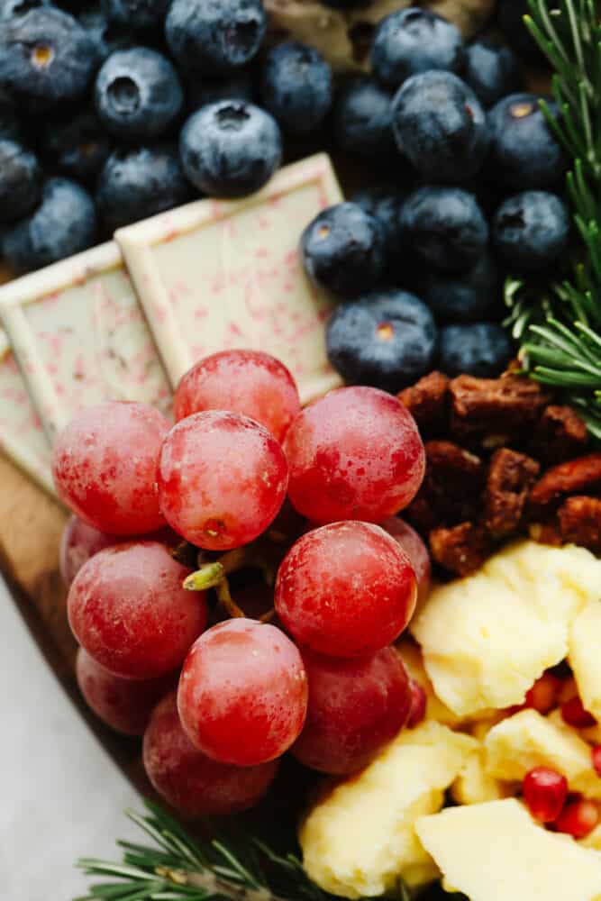 This Christmas wreath charcuterie board is the perfect festive touch to any holiday party! It's stunning and delicious! Plus, it's super easy to make and all of your guests will be so impressed! A close up of some grapes and fruit on the charcuterie board.