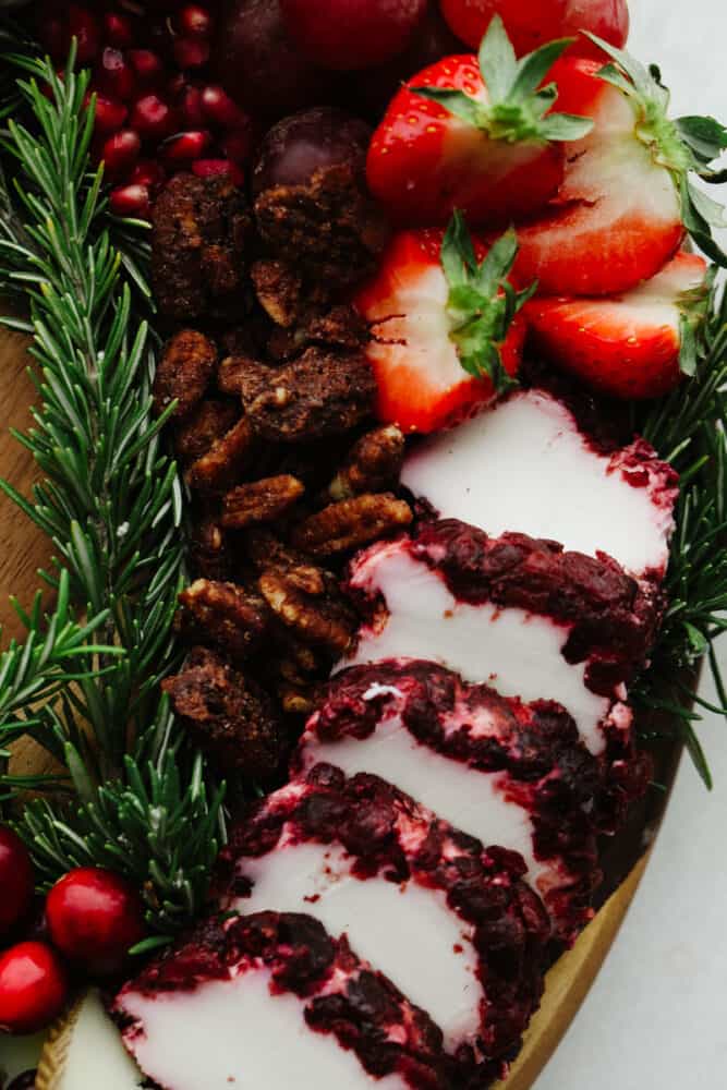 This Christmas wreath charcuterie board is the perfect festive touch to any holiday party! It's stunning and delicious! Plus, it's super easy to make and all of your guests will be so impressed! A close up of some cheese, candied pecans, strawberries and a rosemary sprig.