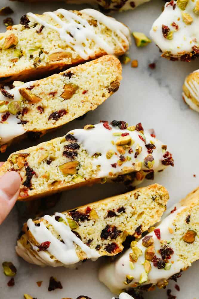 Cranberry pistachio biscotti are the tangy, nutty biscuits of your dreams! Topped off with a delicate white chocolate drizzle, these delicious treats will shine at all of your holiday get-togethers! Closeup of biscotti, dipped in white chocolate and topped with pistachio and cranberry pieces.
