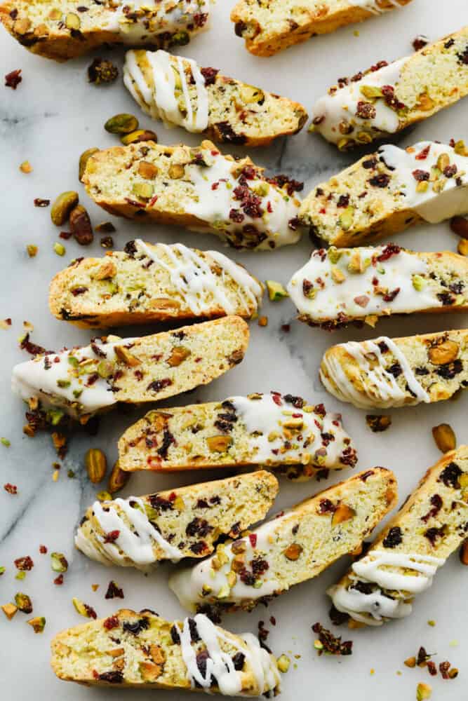 Cranberry pistachio biscotti are the tangy, nutty biscuits of your dreams! Topped off with a delicate white chocolate drizzle, these delicious treats will shine at all of your holiday get-togethers! Biscotti pieces laid out, sprinkled with cranberry and pistachio topping.