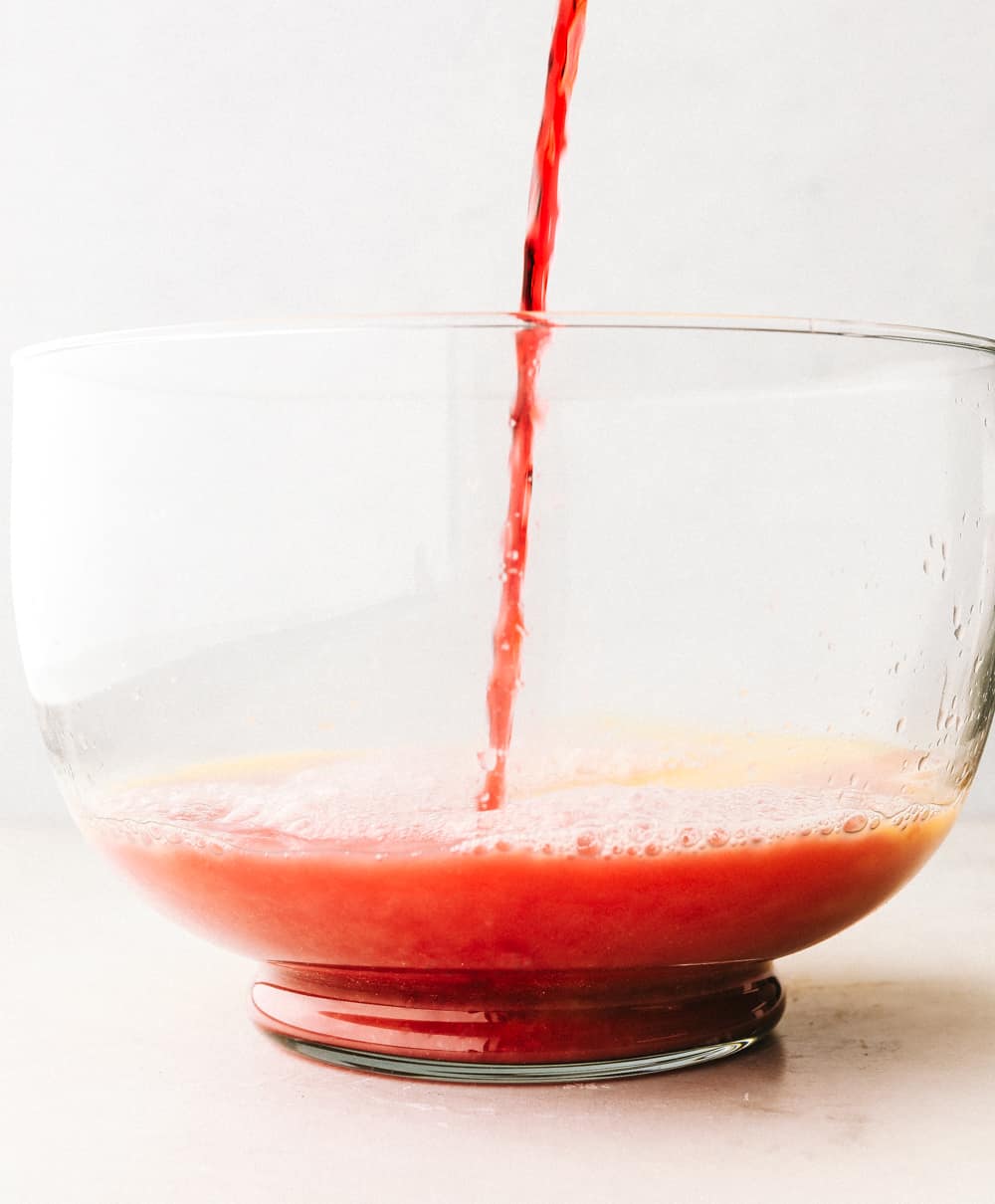 This easy Christmas punch is delicious and so festive! It's the perfect punch to serve at your next gathering. It's for all ages, young and old! Juice being poured into a glass punch bowl.