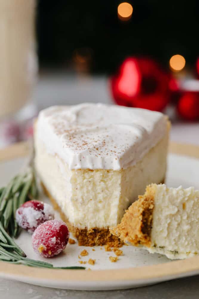 This eggnog cheesecake is SOO GOOD. It's creamy and melts in your mouth! That classic eggnog taste makes it the best dessert for the holiday season! A slice of cheesecake with a fork cutting into it.