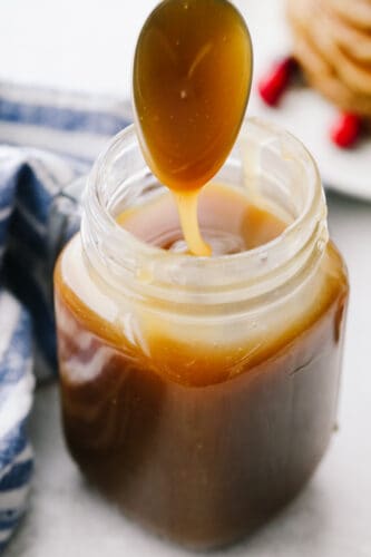 This homemade caramel syrup is the best that you will ever taste! Not only does it have the perfect texture but it is made for drizzling on any and all of your favorite breakfast foods! A jar of caramel syrup with a spoon being dipped into it.