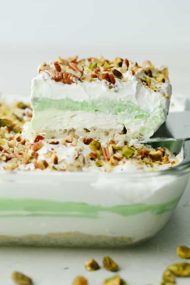 This layered pistachio dessert is insanely delicious! It has the perfect crust that is then topped with layers of creamy cheesecake and pistachio pudding! A slice of pistachio dessert being taken out of a 9x13 baking pan.