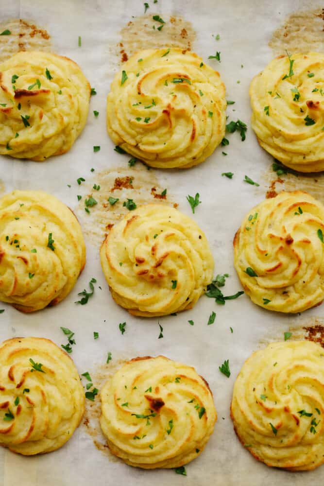 Duchess potatoes are everything you love about mashed potatoes piped into bite-sized pieces! Baked to a golden-brown, this side is absolutely delicious and looks amazing on a dinner plate! Baked duchess potatoes on parchment paper.