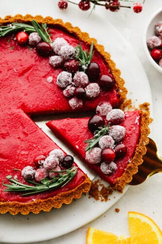 With a smooth tangy filling and Biscoff crust, this cranberry curd tart is a must-make for the holidays. It's as delicious as it is beautiful! Getting a slice of cranberry curd tart with a pie spatula.