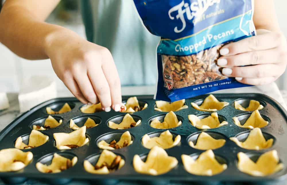 Cranberry pecan brie bites are such an amazing appetizer! It has layered pecans, soft brie, and a dollop of cranberry sauce all cupped in a golden brown, flaky crescent roll! Crescent rolls being placed in a muffin tin sprinkled with pecans.