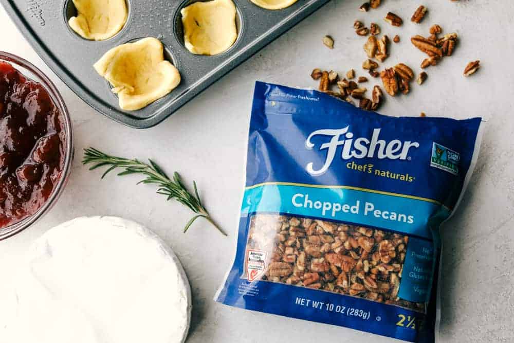 Cranberry pecan brie bites are such an amazing appetizer! It has layered pecans, soft brie, and a dollop of cranberry sauce all cupped in a golden brown, flaky crescent roll! Fisher pecans in a bag next to brie, cranberry sauce and crescent rolls.