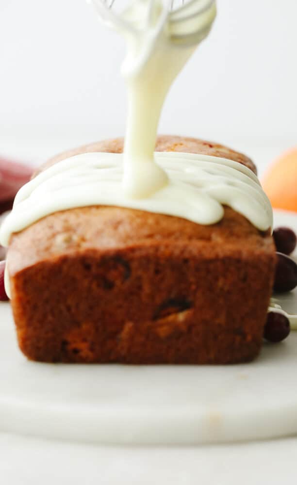 A flavorful quick bread, with hints of citrus and tart cranberries, and topped with an orange glaze. This moist, tender, delicious bread is going to be the hit of your holiday season. A glaze being drizzled on a loaf of bread.
