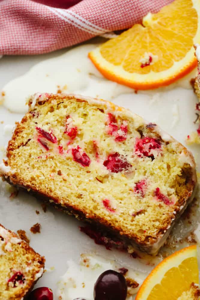 Cranberry orange quick bread is a flavorful quick bread, with hints of citrus and tart cranberries, and topped with an orange glaze. This moist, tender, delicious bread is going to be the hit of your holiday season. A slice of cranberry orange quick bread.