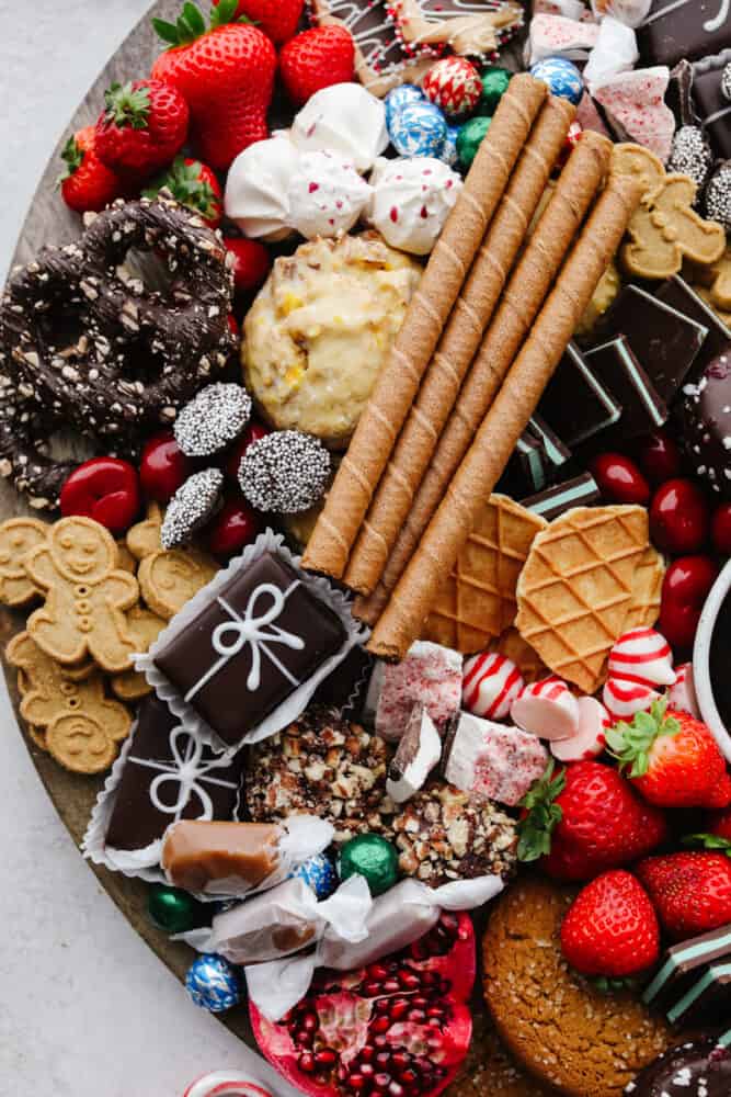 If you are looking for a Christmas dessert to impress your guests then this charcuterie board is it! Stunning and delicious, this board is full of candy, chocolate, cookies, and fruit for the holiday season! A zoomed in shot of some chocolates, cookies, fruit and candy on a wooden board.