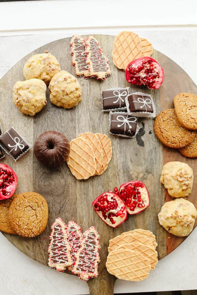 If you are looking for a Christmas dessert to impress your guests then this charcuterie board is it! Stunning and delicious, this board is full of candy, chocolate, cookies, and fruit for the holiday season! A wooden board with pasties being added to it.