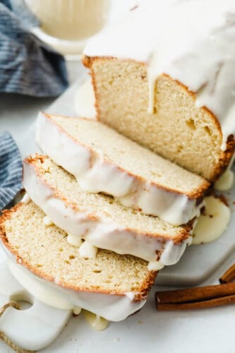 The subtle taste of eggnog in this quick bread is amplified with the ooey-gooey eggnog glaze that is drizzled on top. It's the perfect simple and easy holiday treat! A loaf of eggnog quick bread sliced with an eggnog glaze on top.