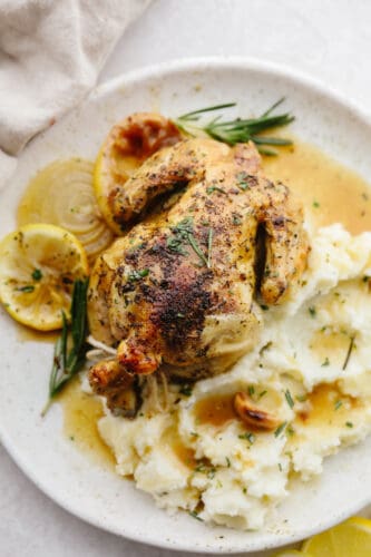 Fancy and baked to crispy perfection these cornish hens will be the star of the show. Not only are they insanely delicious but they are so simple to make! A cooked cornish hen on a plate with some mashed potatoes.