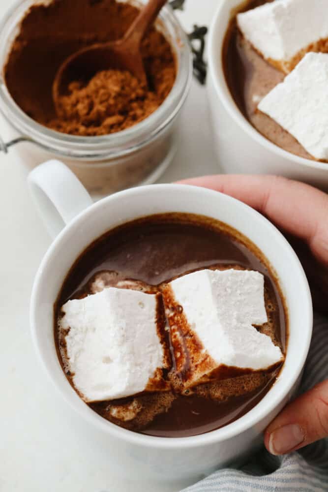 This easy homemade hot chocolate is the perfect treat to end your year with! It's so rich and creamy, you won't want it any other way! Holding a white mug filled with hot chocolate and marshmallows.