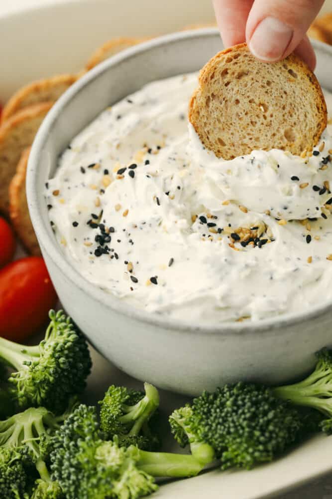 This creamy everything bagel dip is THE BEST dip out there! Bring it as an appetizer that everyone will enjoy and it will fly off of the table! Bread being dipped into everything bagel dip.