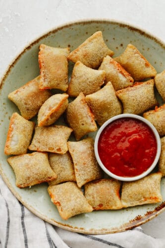 These pizza rolls are cooked to perfection in the air fryer. They take less than 10 minutes and make the perfect lunch or after-school snack. My kids love them! Pizza rolls on a plate with marinara sauce.