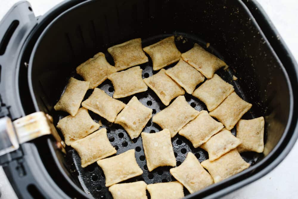These pizza rolls are cooked to perfection in the air fryer. They take less than 10 minutes and make the perfect lunch or after-school snack. My kids love them! Frozen pizza rolls in an air fryer basket about to be cooked.