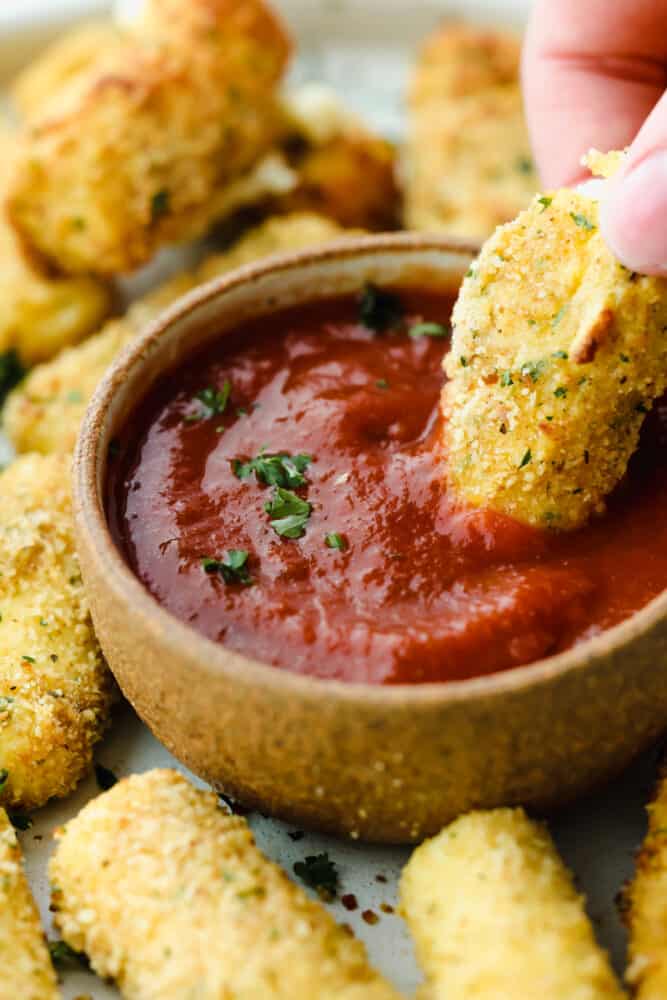 Crispy, cheesy, and delicious, these easy air fryer mozzarella sticks are going to be your new favorite snack! They're super simple to prepare and cook up in less than 10 minutes! Dipping a mozzarella stick into marinara sauce.