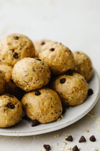 Protein balls are a delicious no-bake treat! Start your new year right by snacking on these tasty, healthy bites loaded with chocolate chips and peanut butter! A white plate stacked with chocolate chip protein balls.