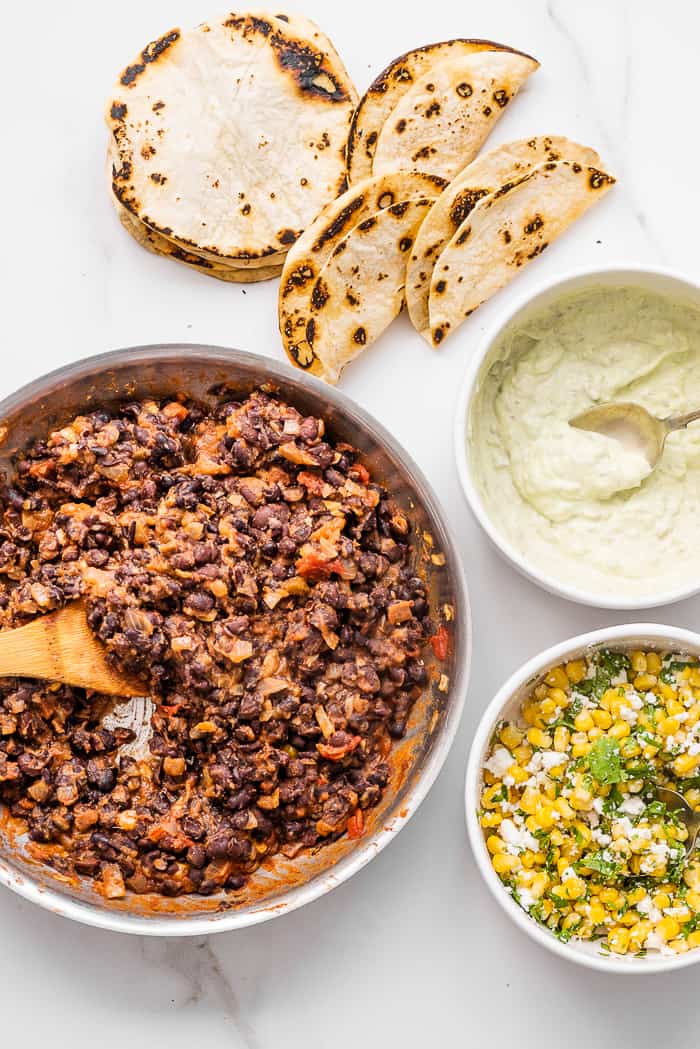 Black bean tacos are an easy-to-make and healthy vegetarian dinner that the whole family will love. Flavorful black beans are spooned inside soft tortillas and topped with simple corn salsa and some avocado crema. the fillings for black bean tacos on a marble countertop