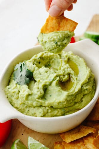 If you are looking for the most delicious appetizer out there, this avocado hummus is for you! Delectable, creamy, and perfect with any veggies or crackers, this dip is the BEST! A bowl of avocado hummus being dipped with a pita chip.