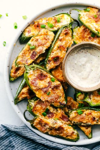 These jalapeño poppers are filled with a cream cheese mixture, topped with crumbled bacon pieces, and then baked to perfection. You won't be able to stop at one! A platter of jalapeño poppers with some dip.