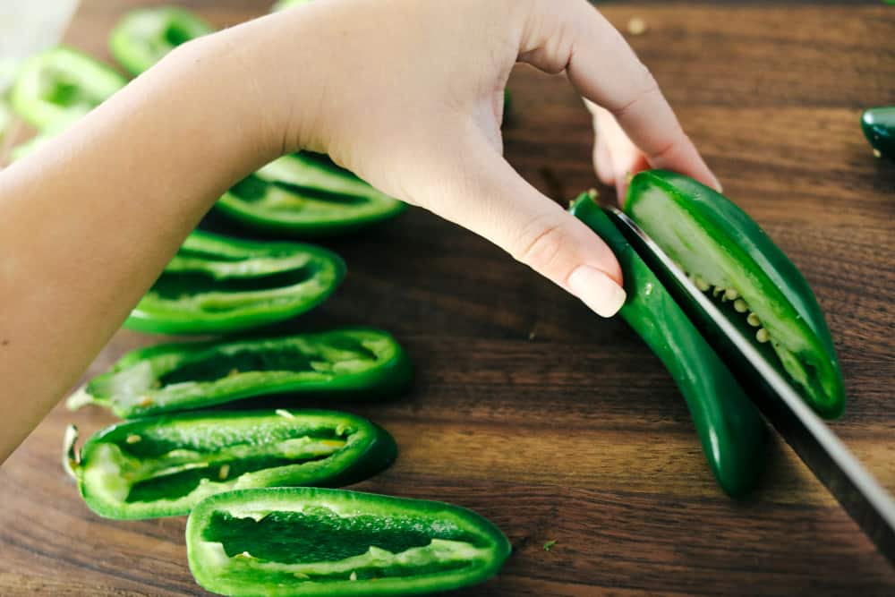 These jalapeño poppers are filled with a cream cheese mixture, topped with crumbled bacon pieces, and then baked to perfection. You won't be able to stop at one! Slicing jalapeño peppers in half.