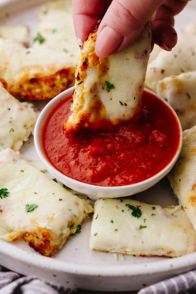 Get your breadstick fix with these to-die-for cauliflower breadsticks! They're smothered in mozzarella and tasty Italian herbs for a snack experience you won't forget. Dipping a breadstick in marinara sauce.