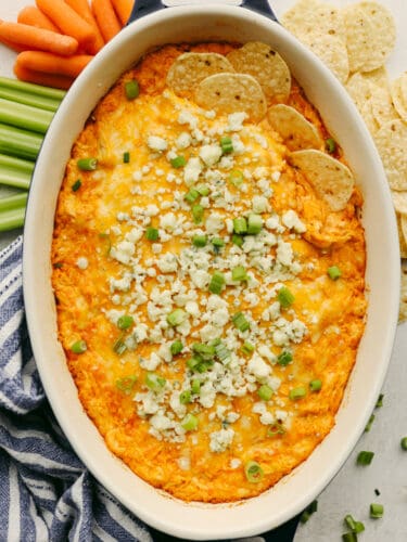 This buffalo chicken dip is the absolute best! Fully loaded with chopped chicken, three types of cheeses, sour cream, and delicious seasonings, this dip has the spicy hot sauce flavor that you are looking for! A dish of buffalo chicken dip with green onions and blue cheese crumbles.