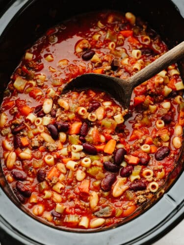 Slow cooker Pasta e Fagioli soup is a rich and hearty Italian soup loaded with pasta, vegetables, beans, and lean ground beef. It's hearty, comforting, and oh so delicious! A crockpot of pasta e fagioli with a wooden spoon.