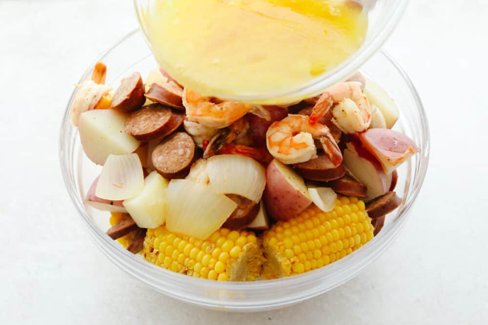 A southern classic, this shrimp boil recipe includes corn, potatoes, sausage, and shrimp boiled together in one pot and packed full of delicious flavor! It's a tried and true favorite that you don't want to miss! Melted butter being poured onto ingredients in a bowl.