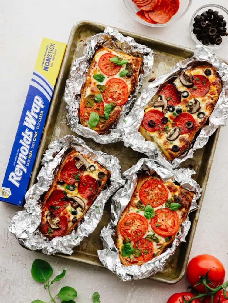These foil french bread pizzas made with Reynolds Wrap® Non-Stick Foil are perfect for any family dinner! Crispy, cheesy, and delicious, your family won't be able to resist coming back for seconds! French bread pizzas wrapped in foil on a baking sheet.