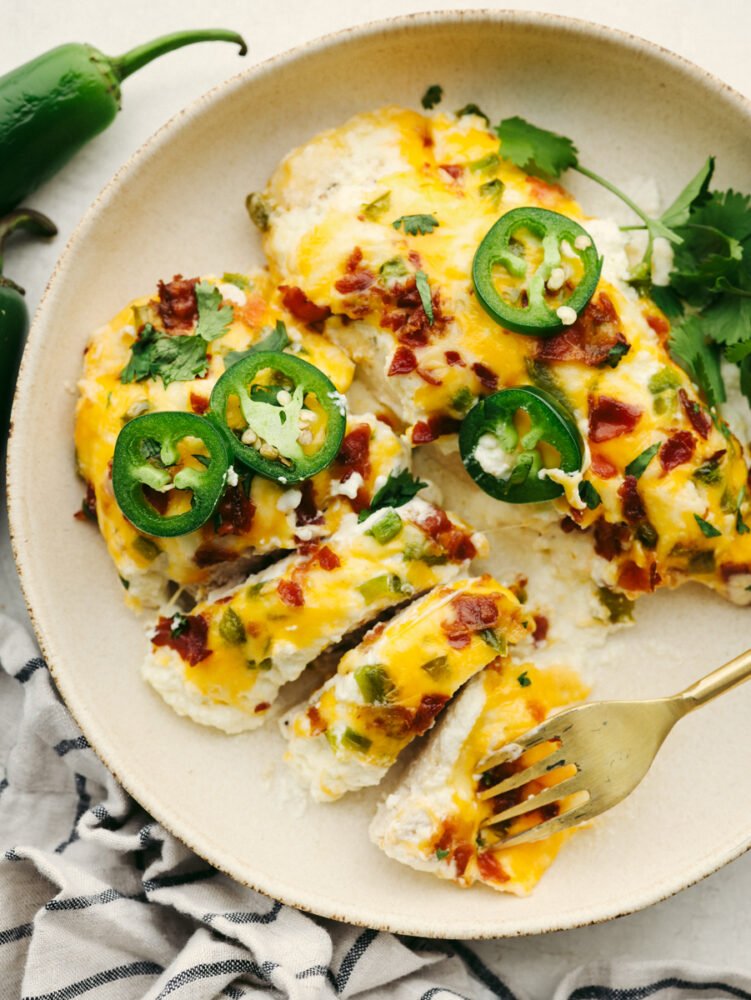 Dinnertime-ready, this jalapeno popper chicken is creamy and delicious with the perfect amount of heat! It has all of the flavors of your favorite appetizers, but in one easy-to-make meal! Two cooked chicken breasts topped with cheese, bacon and jalapenos, one cut into pieces.