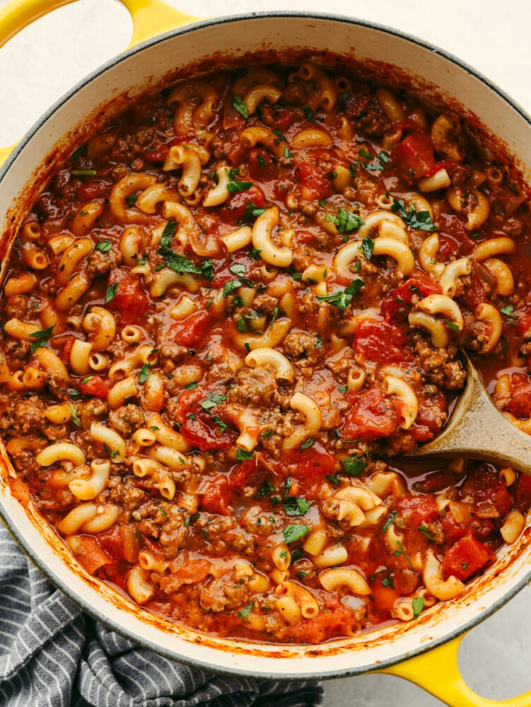 American goulash is an easy, old-fashioned, and comforting meal that is insanely delicious and perfect for the cold winter months. Everything cooks in one pot, even the pasta! A pot of American goulash with a wooden spoon in it.