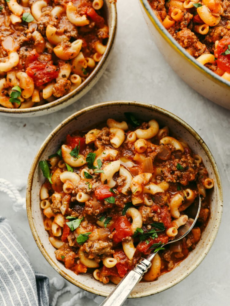 American goulash is an easy, old-fashioned, and comforting meal that is insanely delicious and perfect for the cold winter months. Everything cooks in one pot, even the pasta! 3 bowls of American goulash, each with a spoon.