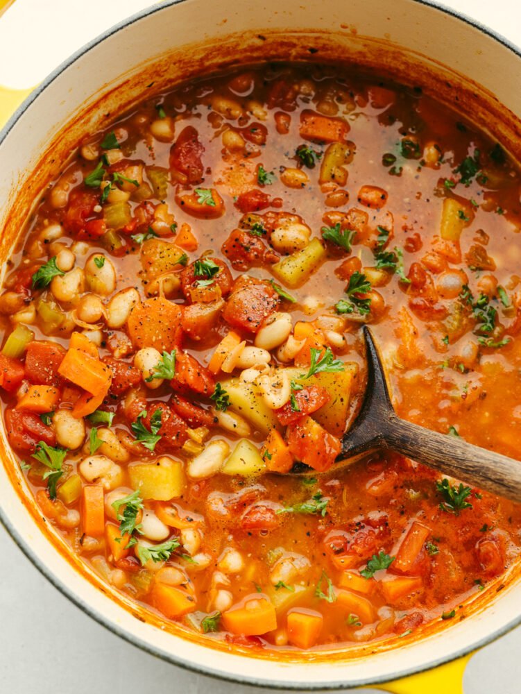 This white bean stew is a classic recipe that will fill your belly and warm you right up! With the insanely delicious flavor, this hearty stew will be your guests' favorite and fly off the table! A pot filled with bean stew and a wooden serving spoon.