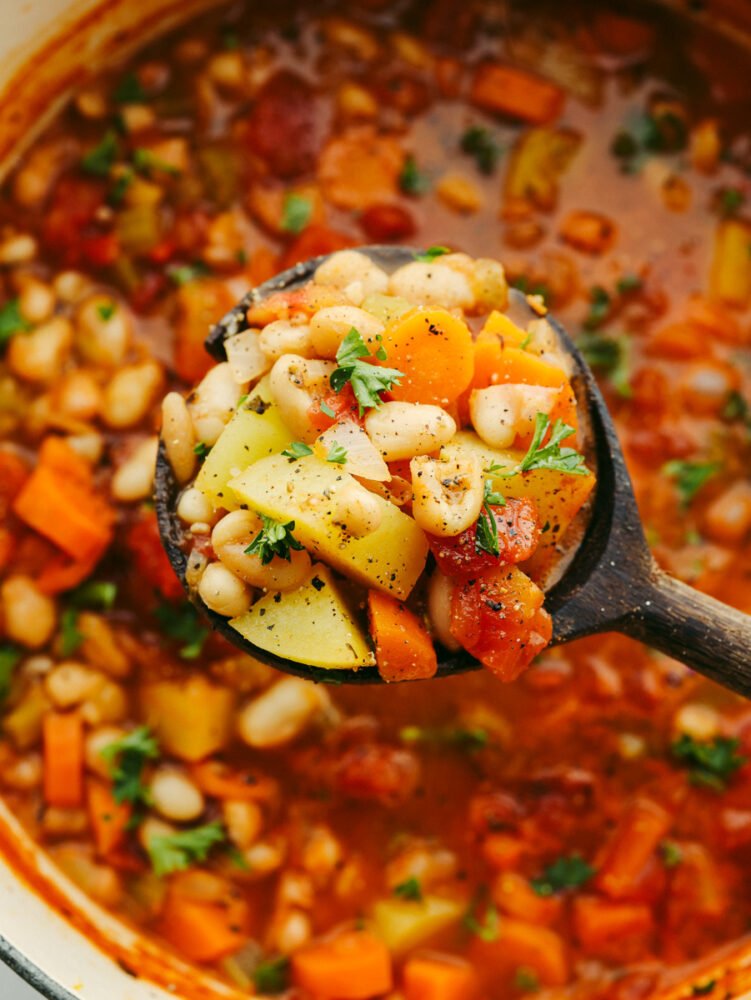 This white bean stew is a classic recipe that will fill your belly and warm you right up! With the insanely delicious flavor, this hearty stew will be your guests' favorite and fly off the table! A wooden spoon filled with bean stew.