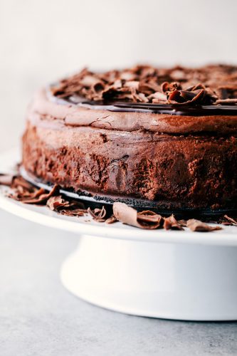 Death by chocolate cheesecake has an Oreo crust with creamy, decadent, and rich chocolate cheesecake. Topped with chocolate ganache, this is a chocolate lover's dream come true! Death by Chocolate Cheesecake on a cake stand.