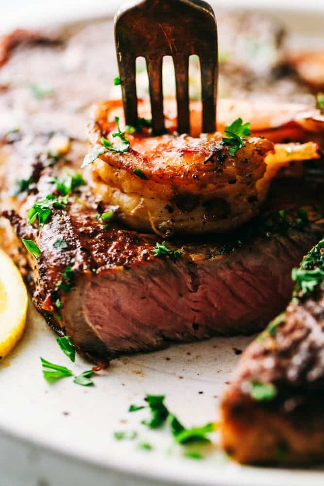 Skillet garlic butter steak and shrimp is pan-seared to tender and juicy perfection and slathered in garlic herb butter. This will be the best steak and shrimp that you EVER make! Steak and shrimp bites on a fork.