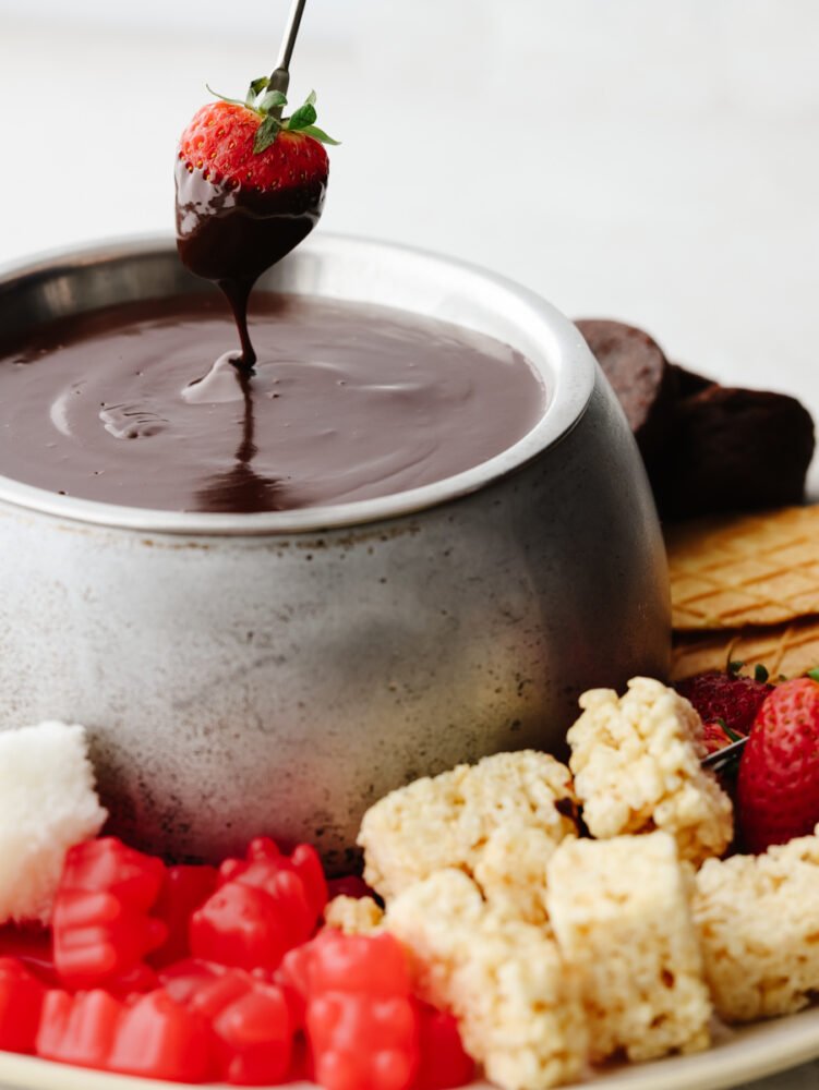 The best way to impress your valentine is with homemade chocolate fondue! This silky-smooth dessert is so amazing and pairs perfectly with all of your favorite treats! A strawberry being dipped into chocolate fondue.