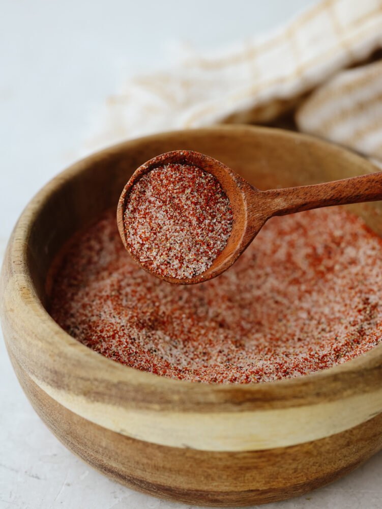 This recipe for homemade seasoning salt will have you making this from scratch and never buying it at the store again! It has the perfect amount of flavor that is ideal for adding to any dish! A wooden bowl filled with mixed seasoning salt and being scooped by a wooden spoon.