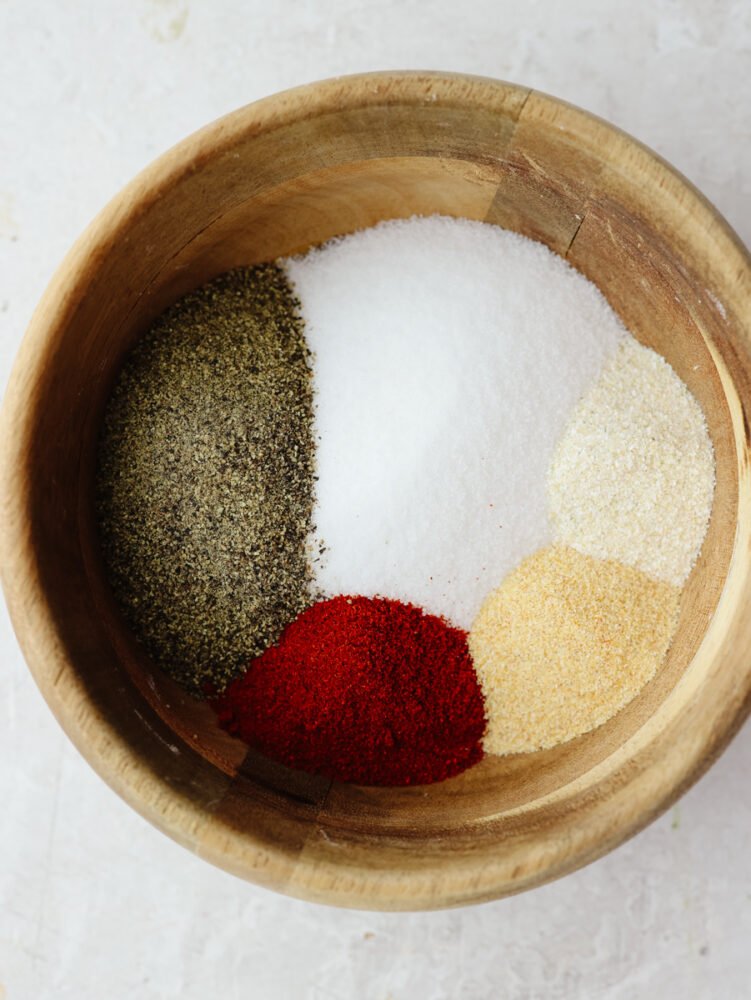 This recipe for homemade seasoning salt will have you making this from scratch and never buying it at the store again! It has the perfect amount of flavor that is ideal for adding to any dish! A wooden bowl filled with spices and seasonings, ready to be mixed together.