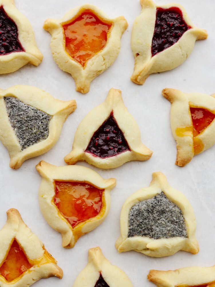 These triangle-shaped hamantaschen cookies are perfectly soft and filled with delicious jams and a homemade poppyseed filling. Step up your game and impress your guests with this unique and flavorful dessert! Hamantaschen baked and ready to eat.