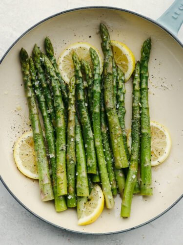 Steamed asparagus is the perfect addition to any meal! All it needs is a squeeze of lemon and freshly cracked salt and pepper to be a knockout side! Steamed asparagus, garnished with lemon, on a white and blue plate.