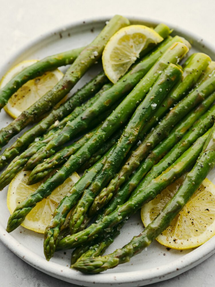 Steamed asparagus is the perfect addition to any meal! All it needs is a squeeze of lemon and freshly cracked salt and pepper to be a knockout side! Closeup of steamed asparagus, garnished with salt, pepper, and lemon.