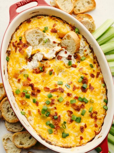 You won't find a better dip out there than this crack chicken dip! It's cheesy and packed with chicken, and bacon and seasoned to perfection. It will be the best appetizer dip that you've ever had! Crack chicken dip baked in a pan and being dipped with bread.