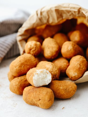 Irish potato candy is a no-bake treat filled with cream cheese and coconut flakes and then topped with cinnamon. These aren't your regular potatoes, they are candy, and I am here for it! A paper bag on its side spilling out Irish potato candy.